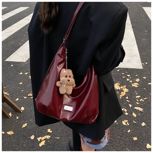 Close-up of a glossy burgundy hobo bag with adjustable strap and a plush bear charm