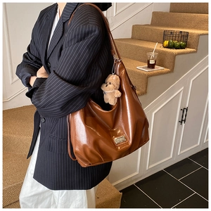 Detailed close-up of a large caramel hobo bag with glossy texture and teddy bear charm