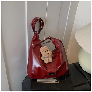 Detail shot of a burgundy glossy tote bag with teddy bear pendant and metal logo plate