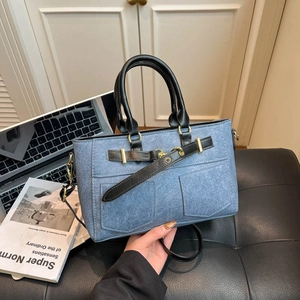 Blue denim handbag with front pockets and black leather straps on an office desk