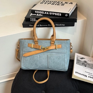 Light blue denim handbag with camel leather straps and gold metal clasp on a black base