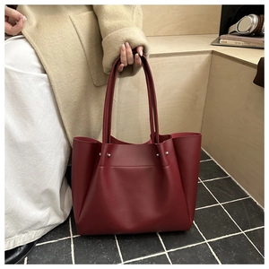 Detail of burgundy tote bag showing soft matte leather texture and rivet accents