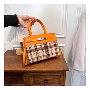 Dettaglio della borsa in pelle arancione e tweed con chiusura in metallo e manici