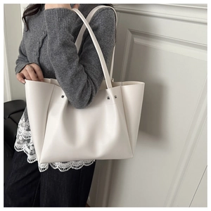 Detailed view of large white leather tote bag with rivets shown on woman's shoulder