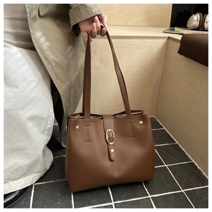 Detail view of large brown leather tote bag with gold oval buckle and rivets