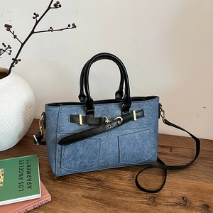 Denim blue patchwork tote bag with black handles and gold hardware on a wooden table