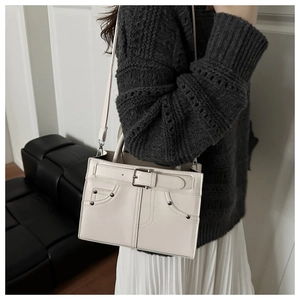 Detail of ivory rectangle crossbody bag with buckle belt and rivet accents on a model