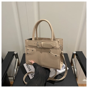 Detail of minimalist cream crossbody bag with metal studs and top handle on a chair