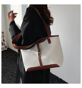 Detail of a large woven texture tote bag with brown leather trim and gold metal buckle