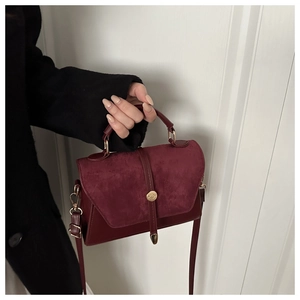 Détail du sac à main bordeaux en daim avec boucle dorée et finitions sophistiquées