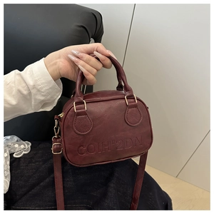 Close-up of a burgundy mini shell bag with gold hardware and embossed lettering detail