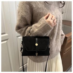 Détail du sac bandoulière en daim noir avec boucle dorée porté par un mannequin