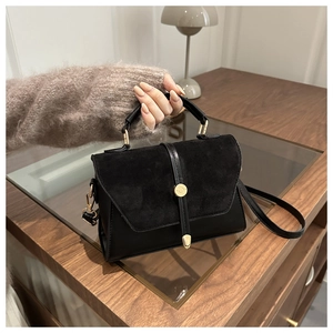 Détail du sac bandoulière en daim noir avec un fermoir doré rond en métal élégant