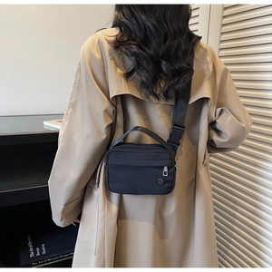 Détail du sac à bandoulière en nylon noir porté par un mannequin en trench-coat beige