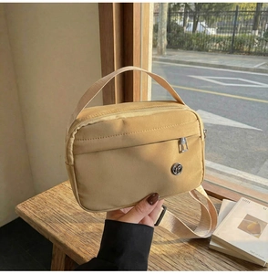 Détail du sac bandoulière en nylon marron clair avec poche zippée et plaque logo en métal