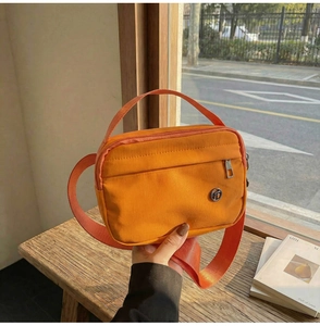 Détail d'un sac à bandoulière orange avec fermeture éclair et logo métallique rond