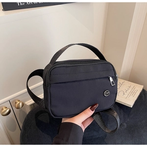 Détail du sac bandoulière en nylon noir avec doubles poches et logo métallique rond