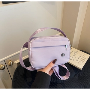 Détail du sac bandoulière en nylon lavande avec logo métallique et poche zippée avant