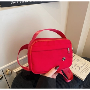 Détail du sac bandoulière en nylon rouge avec large sangle et poche frontale zippée