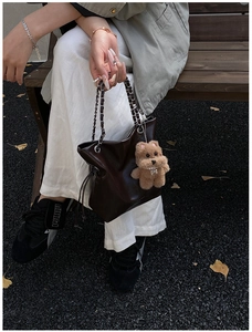 Detail of dark brown leather bucket bag with chain strap and cute bear plush pendant
