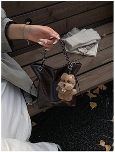 Detail of dark brown leather bucket bag with chain handle and plush bear charm