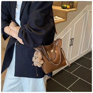 Détail du sac seau en cuir marron avec chaîne en métal et pendentif ours en peluche