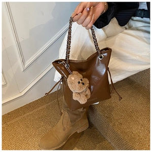 Detail of a brown bucket bag with a chain handle, drawstring, and cute teddy bear charm