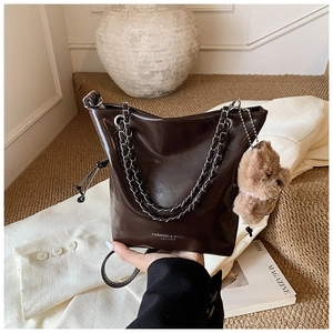 Detail of dark brown glossy leather bucket bag with chain strap and teddy bear charm