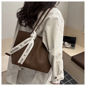 Dettaglio della borsa tote in pelle marrone scuro con nastro bianco stampato sul manico