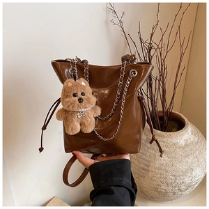 Close-up of dark brown glossy bucket bag with silver chain and cute teddy bear charm