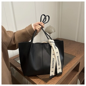 Dettaglio di una borsa tote in pelle nera opaca con nastro decorativo su un mobile in legno