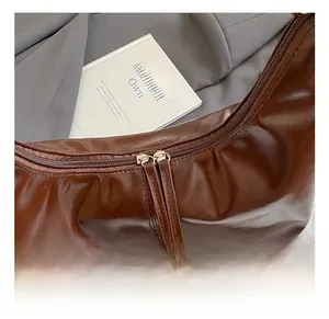 Detail of dark brown glossy leather crescent bag with dual zippers and long leather pulls