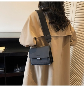 Close-up of minimalist black crossbody bag with wide fabric strap on a beige coat