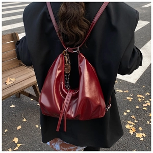 Detail of dark red patent leather tote bag with a golden tennis racket charm outdoors