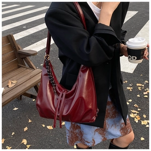 Detail of burgundy oversized hobo bag in soft faux leather with side tassel and slim strap