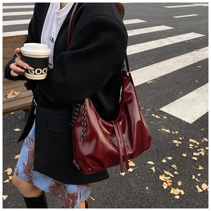 Macro detail of deep red glossy hobo bag with trendy pleats and tassel hanging