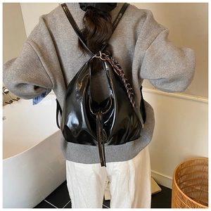 Detail of black patent leather tote bag with glossy texture and striped webbing strap