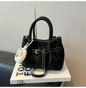 Detail of black suede handbag with white stitching and plush cartoon charm on a book