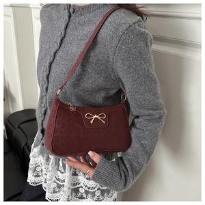 Close-up of burgundy shoulder bag featuring a golden bow and flower zipper detail