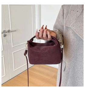 Detail of burgundy mini crossbody bag featuring golden metal buckles and top handle