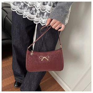 Close-up of a burgundy leopard print underarm bag featuring a golden bow and floral charm