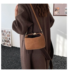 Close-up of brown suede shoulder bag with gold metal clasp on wool coat background