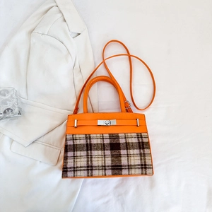 Detail of orange leather and plaid fabric texture with a silver twist-lock clasp on bag