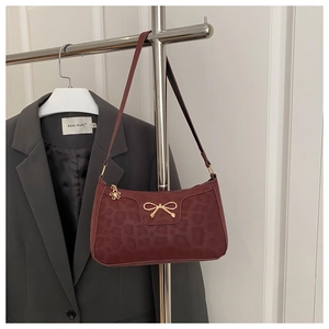 Detail of burgundy baguette bag featuring leopard texture and gold bow charm detail