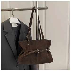 Detail of dark brown retro tote bag with silver eyelets and buckle on gray blazer