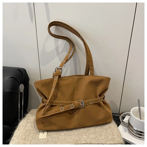 Detailed view of brown biker-style underarm bag with decorative belt on beige cushion
