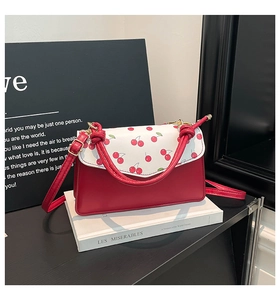 Detail of red and white cherry print handbag with knotted handle on a book