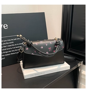 Close-up of matte black crossbody bag with floral bow print on textured book background