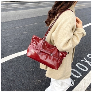 Streetstyle opname van een vrouw met een donkerrode laks leren tas over een beige jas