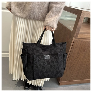 Detail of black jacquard tote bag with floral texture and side pockets on wooden background